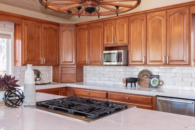 kitchen featuring stainless steel appliances, brown cabinetry, and light countertops