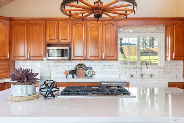 kitchen featuring decorative backsplash, brown cabinets, stainless steel appliances, light countertops, and a sink