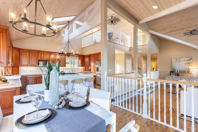 dining space with vaulted ceiling with beams, wooden ceiling, light wood-style flooring, and ceiling fan with notable chandelier