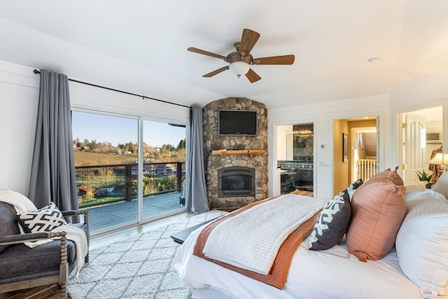 bedroom featuring lofted ceiling, ceiling fan, a stone fireplace, wood finished floors, and access to outside