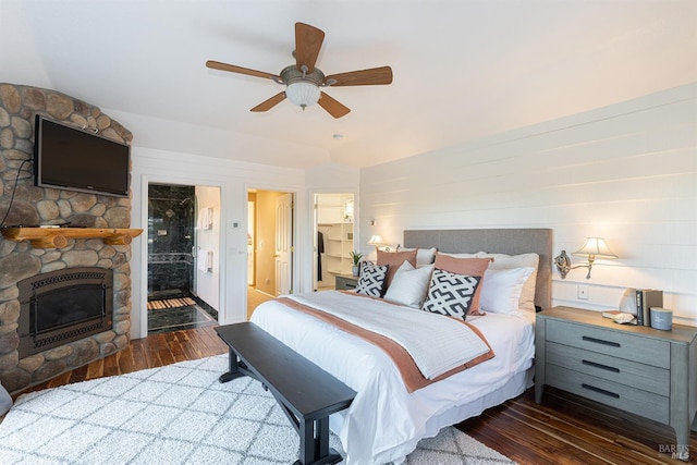 bedroom with ensuite bathroom, dark wood-style flooring, a fireplace, and a ceiling fan