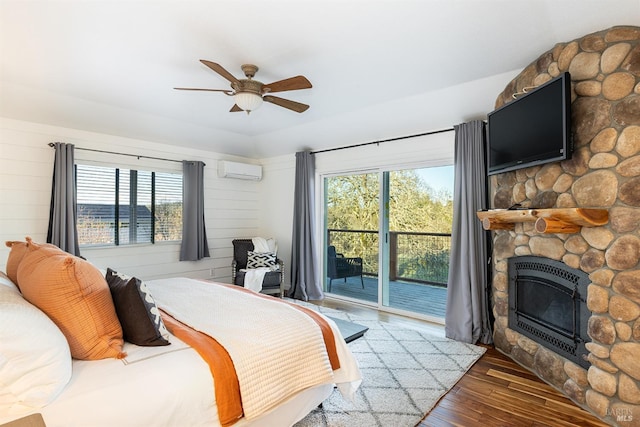 bedroom with ceiling fan, a fireplace, wood finished floors, access to exterior, and a wall mounted air conditioner