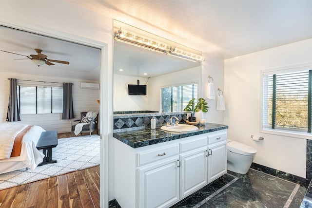 ensuite bathroom featuring baseboards, toilet, ceiling fan, wood finished floors, and vanity