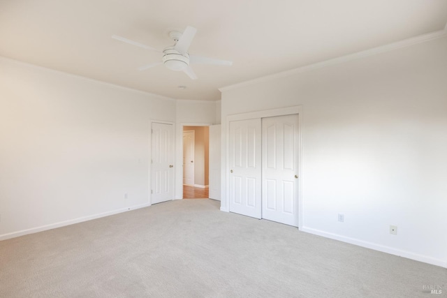 unfurnished bedroom featuring ceiling fan, light colored carpet, baseboards, ornamental molding, and a closet