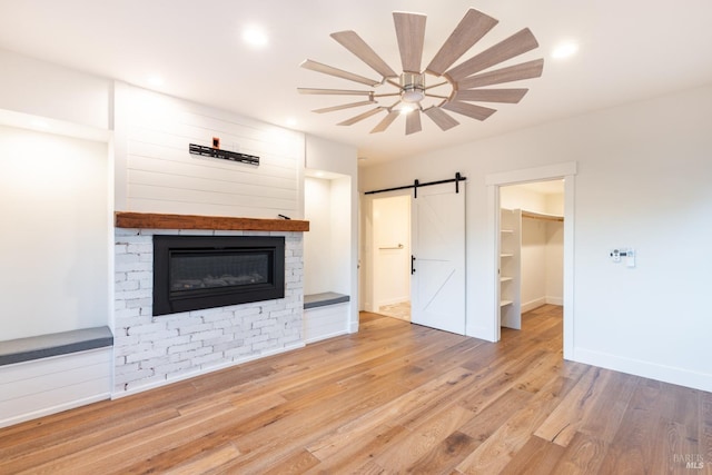 unfurnished living room with a barn door, a glass covered fireplace, ceiling fan, wood finished floors, and baseboards