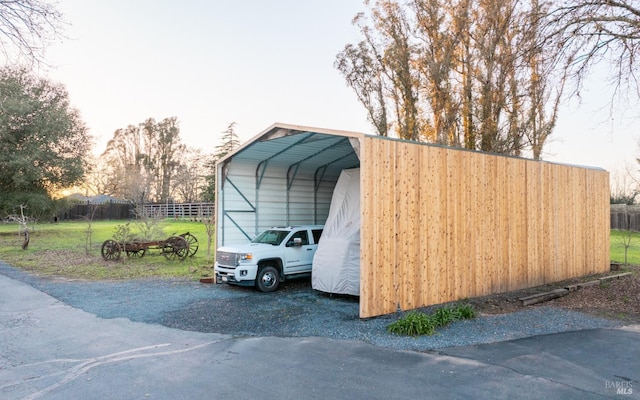 view of outbuilding with a detached carport, fence, and driveway