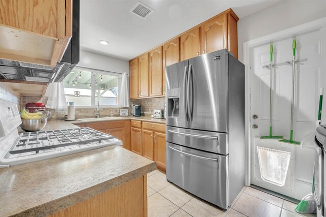 kitchen with light countertops, light tile patterned floors, a sink, stainless steel fridge, and tasteful backsplash