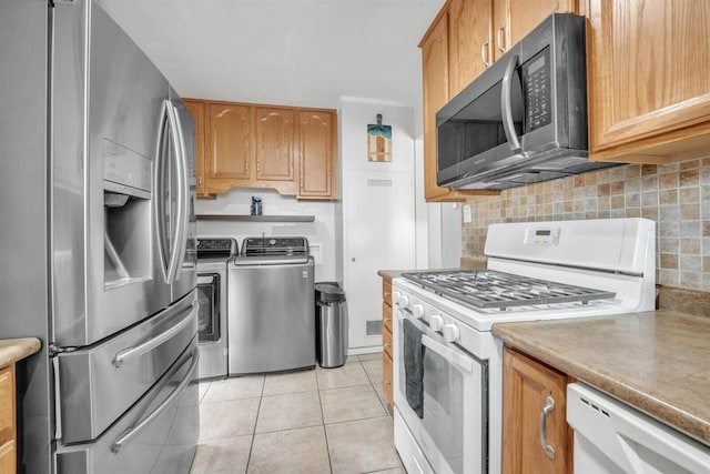 kitchen featuring light tile patterned flooring, decorative backsplash, brown cabinetry, washer and dryer, and appliances with stainless steel finishes