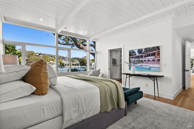 bedroom with a water view, a walk in closet, wood ceiling, beam ceiling, and hardwood / wood-style floors