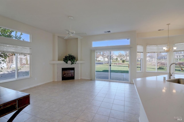 living room with a tiled fireplace, ceiling fan with notable chandelier, sink, and light tile patterned floors