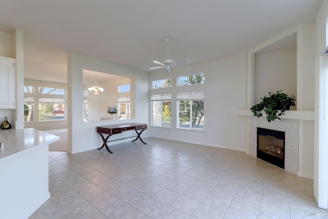 interior space featuring a tiled fireplace, light tile patterned flooring, and ceiling fan with notable chandelier