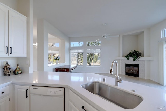 kitchen featuring a sink, dishwasher, ceiling fan, a fireplace, and white cabinets