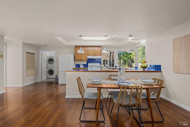 dining space featuring baseboards, a tray ceiling, dark wood finished floors, and stacked washer / drying machine