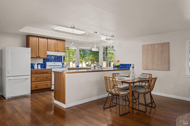 kitchen featuring white appliances, a raised ceiling, hanging light fixtures, and dark wood-style flooring