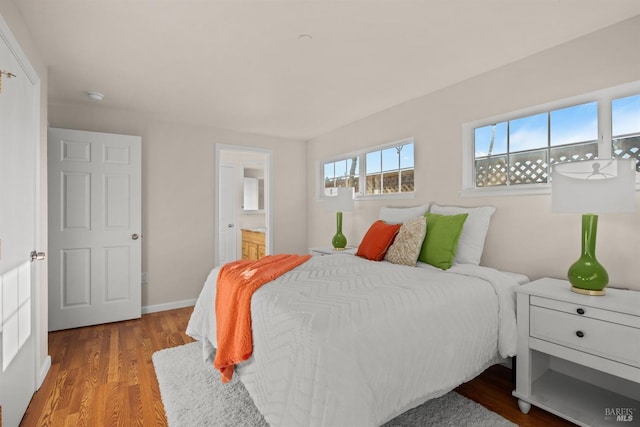 bedroom with ensuite bath, baseboards, and wood finished floors