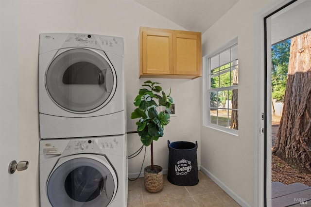 clothes washing area featuring light tile patterned floors, baseboards, cabinet space, and stacked washer / drying machine