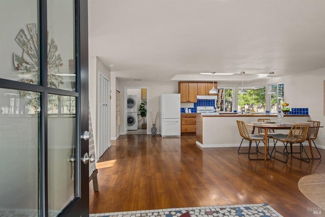 interior space featuring dark wood-type flooring, stacked washer / dryer, freestanding refrigerator, brown cabinetry, and decorative light fixtures