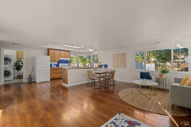 living area featuring dark wood-type flooring, stacked washer / dryer, and baseboards