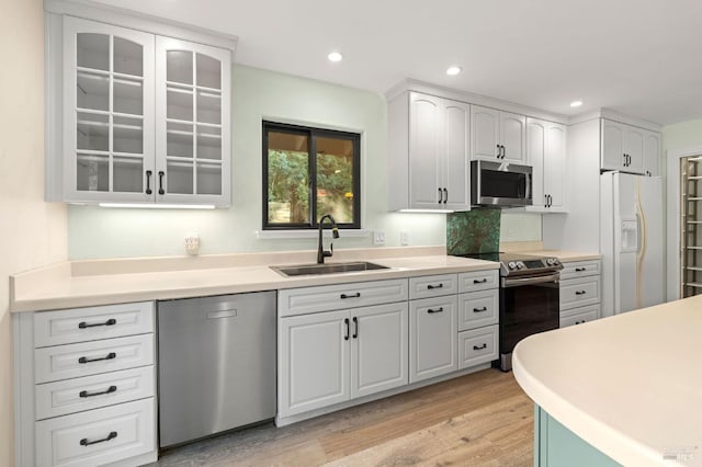 kitchen featuring glass insert cabinets, white cabinetry, stainless steel appliances, light wood finished floors, and a sink