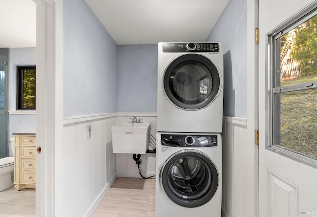 laundry area featuring stacked washer and dryer, wainscoting, a sink, and laundry area