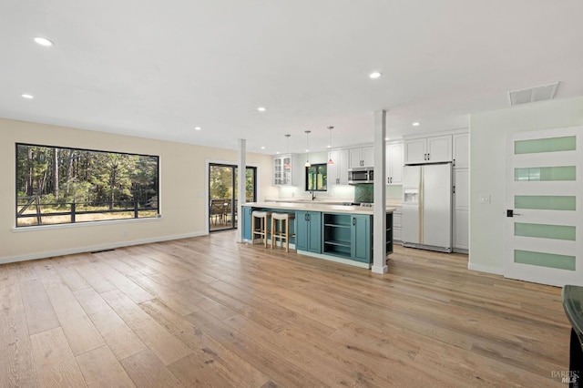 kitchen with white cabinets, a kitchen island, light countertops, white fridge with ice dispenser, and pendant lighting