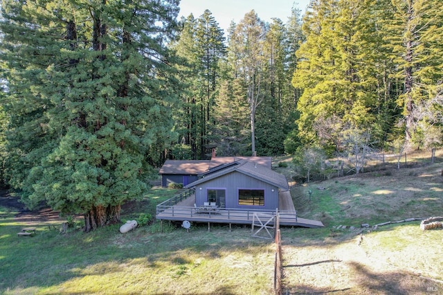 rear view of house with a yard, a wooden deck, and a view of trees