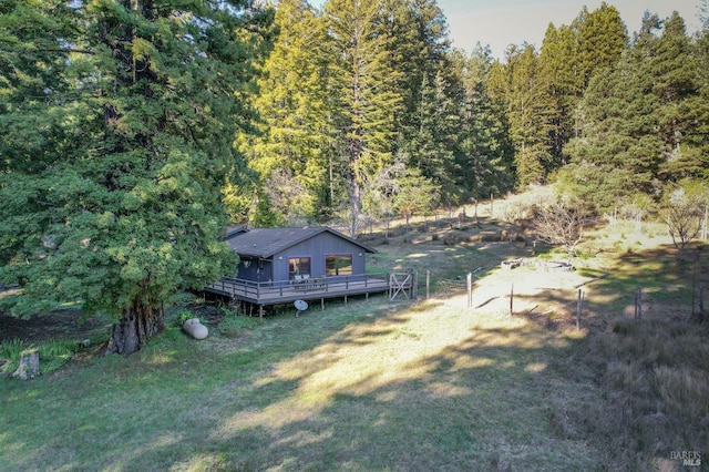 exterior space with a rural view, a deck, a wooded view, and a yard