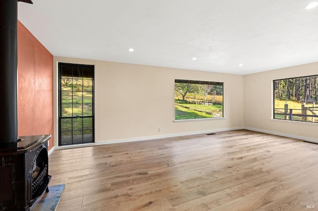 living area with plenty of natural light, light wood-type flooring, a wood stove, and baseboards