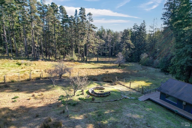 view of yard with a wooded view, fence, and an outdoor fire pit