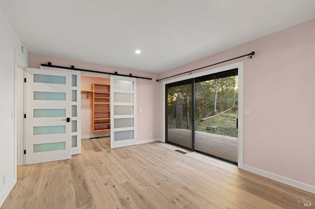 empty room with a barn door, light wood-type flooring, visible vents, and baseboards