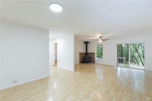 unfurnished living room featuring light wood-type flooring, ceiling fan, and a wood stove