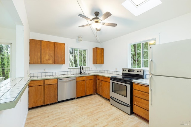 kitchen with sink, light hardwood / wood-style flooring, appliances with stainless steel finishes, tile countertops, and kitchen peninsula