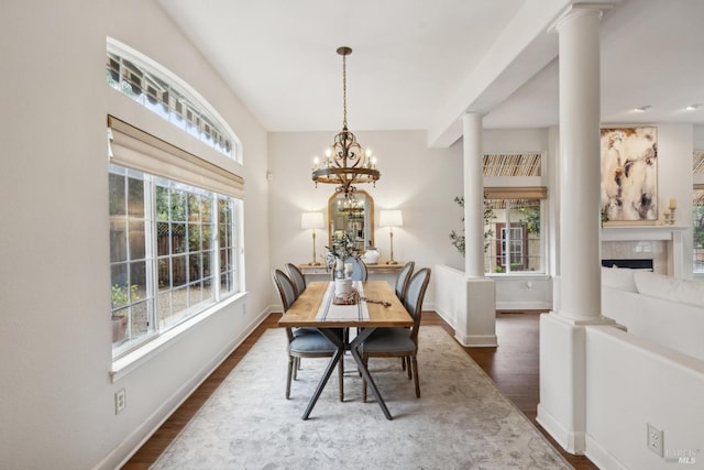 dining area featuring ornate columns, a tile fireplace, a notable chandelier, and dark hardwood / wood-style flooring