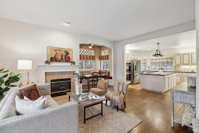 living room with ceiling fan, a tiled fireplace, and light wood-type flooring