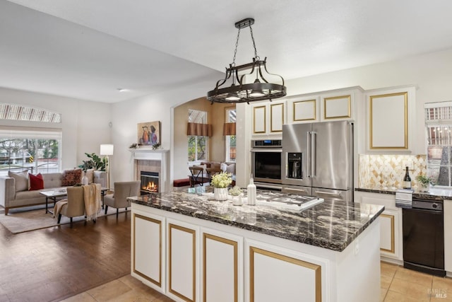 kitchen with decorative light fixtures, dark stone countertops, a kitchen island, stainless steel appliances, and cream cabinetry