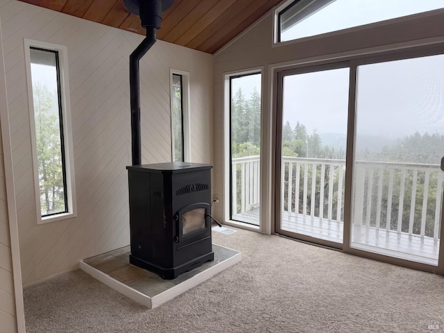 doorway to outside with vaulted ceiling, carpet, a wood stove, and wooden walls