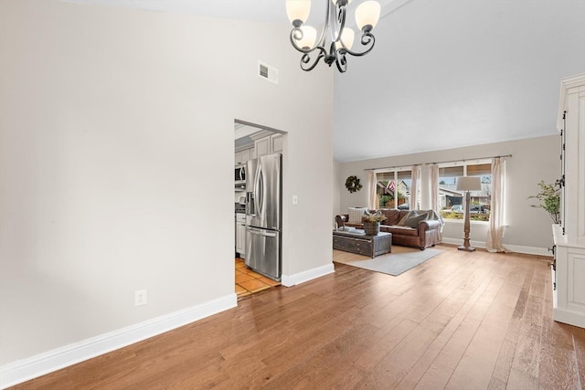 unfurnished living room featuring light wood-type flooring, an inviting chandelier, baseboards, and visible vents