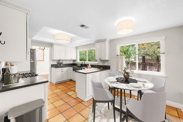 kitchen featuring a sink, visible vents, white cabinets, a tray ceiling, and dark countertops