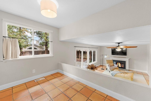 interior space with light tile patterned floors, visible vents, baseboards, a glass covered fireplace, and ceiling fan