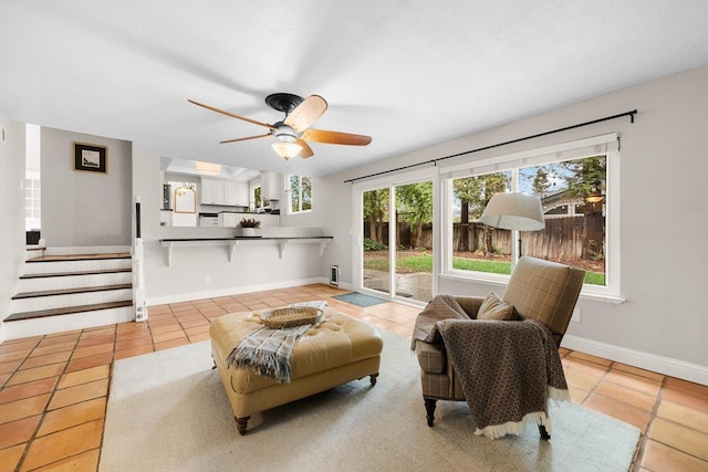 tiled living area featuring ceiling fan, baseboards, and stairs