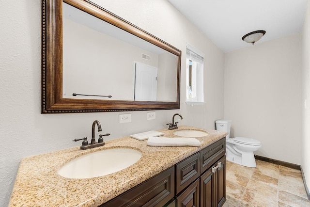 bathroom with toilet, double vanity, visible vents, and a sink