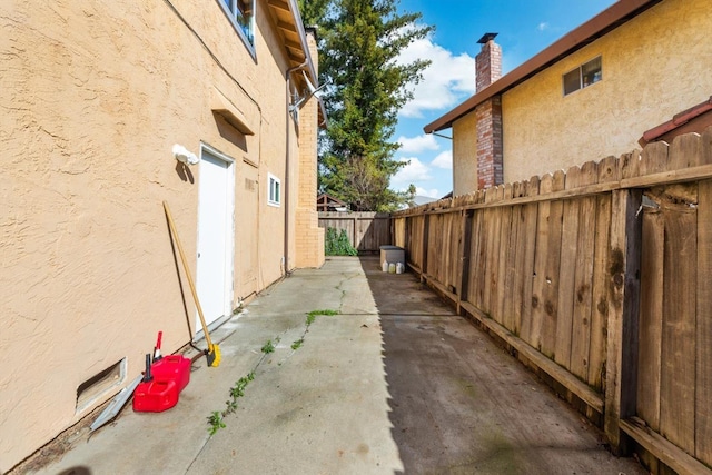 view of side of home with a patio area, a chimney, fence, and stucco siding