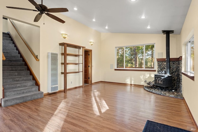 unfurnished living room with light hardwood / wood-style flooring, high vaulted ceiling, ceiling fan, and a wood stove