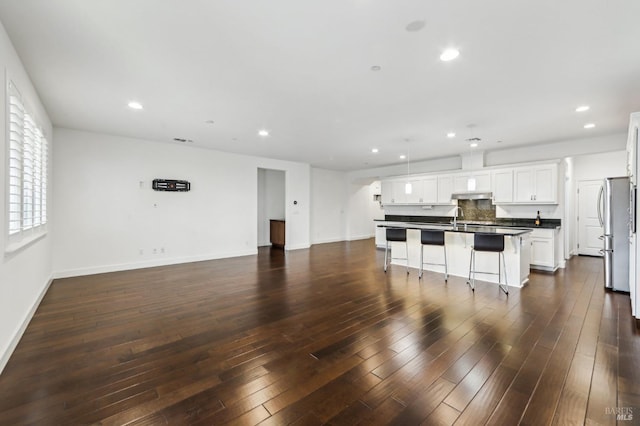 kitchen with dark wood-type flooring, stainless steel fridge, white cabinetry, a kitchen breakfast bar, and a kitchen island