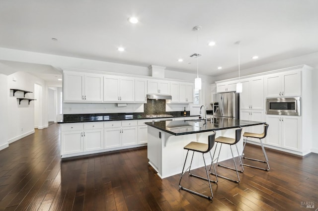 kitchen featuring stainless steel appliances, a center island with sink, white cabinets, and decorative light fixtures