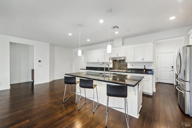 kitchen featuring a kitchen island with sink, hanging light fixtures, white cabinetry, and stainless steel refrigerator