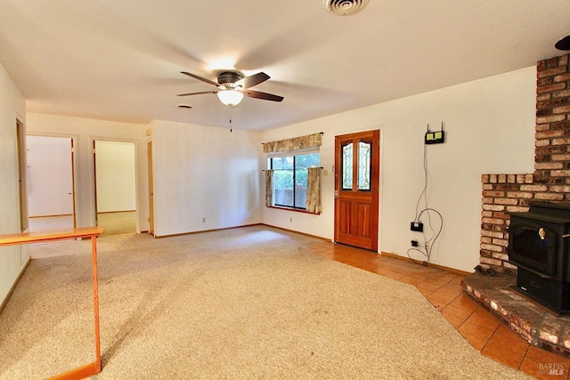 unfurnished living room with tile patterned flooring, visible vents, baseboards, a ceiling fan, and a wood stove