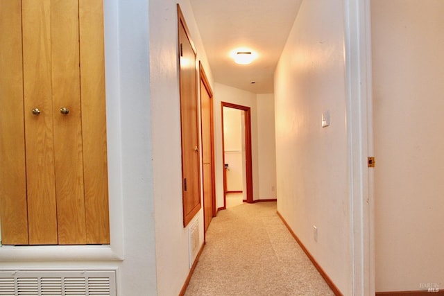 hallway with light colored carpet, visible vents, and baseboards