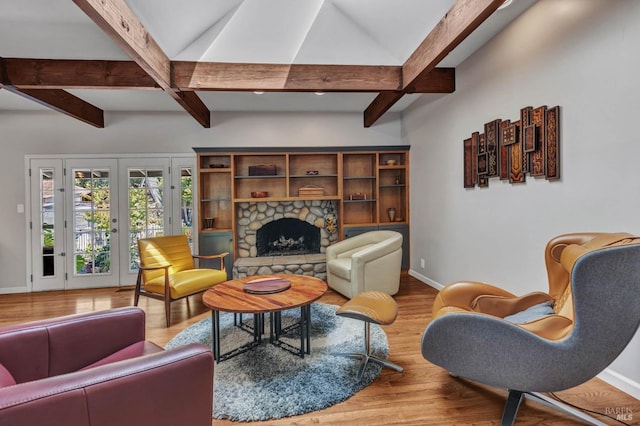 living area with beamed ceiling, a stone fireplace, baseboards, and wood finished floors