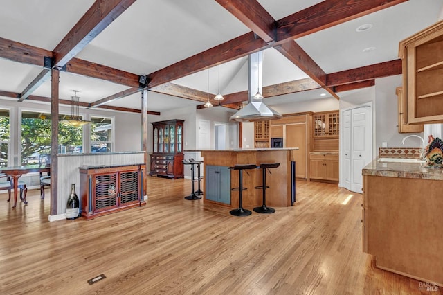 kitchen with light wood finished floors, glass insert cabinets, beamed ceiling, a kitchen bar, and a sink